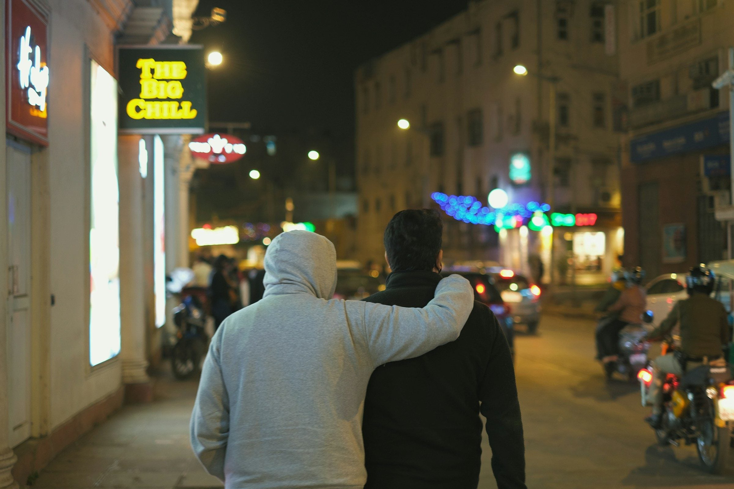 Two people walking home together down a lit street at night